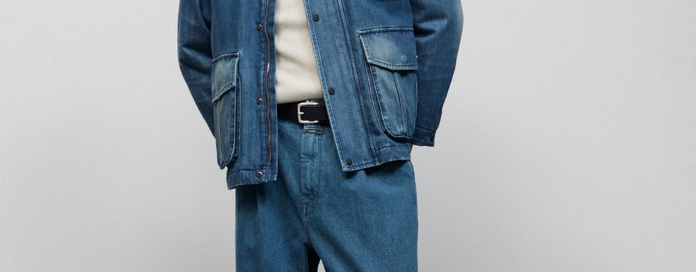 Man sieht die Körpermitte eines männlichen Models, welches eine blaue Jeansjacke mit aufgesetzten Taschen, sowie eine farblich passende Jeans von Closed trägt.