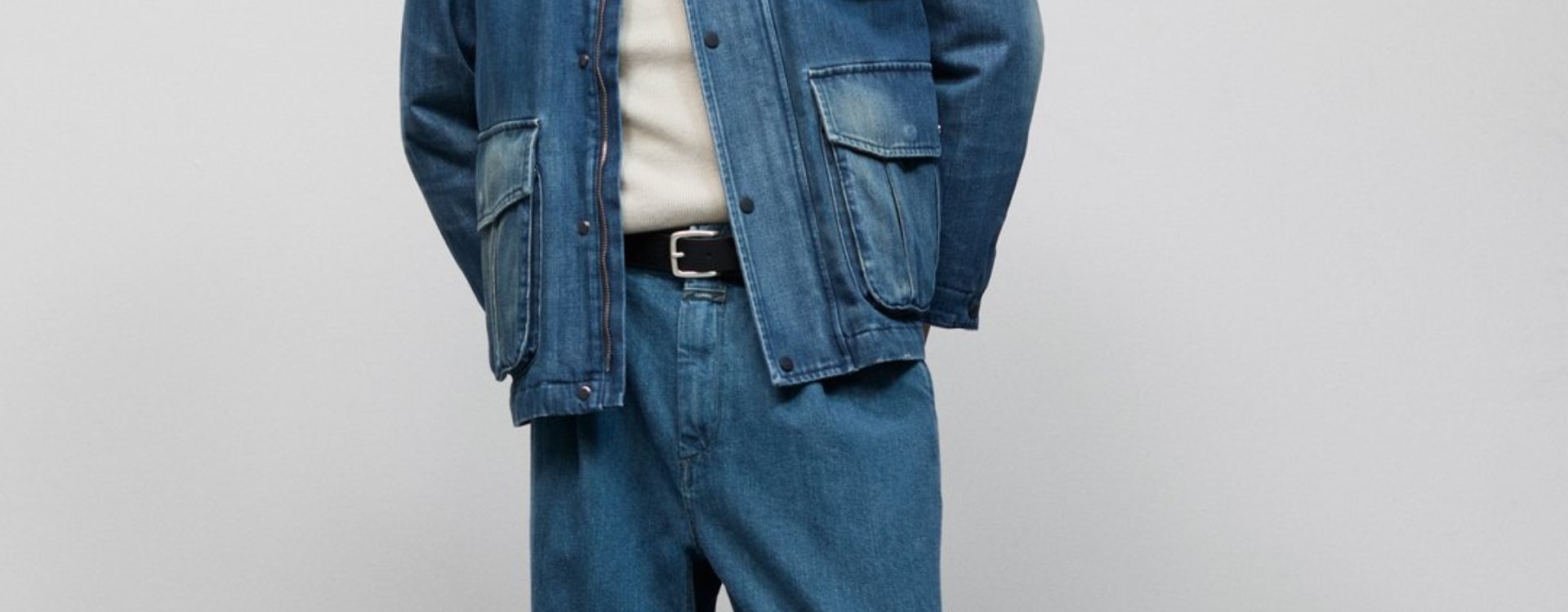 Man sieht die Körpermitte eines männlichen Models, welches eine blaue Jeansjacke mit aufgesetzten Taschen, sowie eine farblich passende Jeans von Closed trägt.