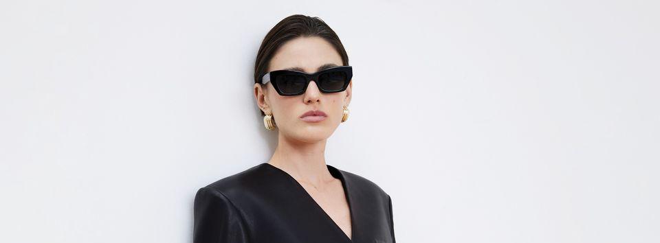 Eine Frau in schwarzer Kleidung mit schwarzer Sonnenbrille und goldenen Ohrringen 