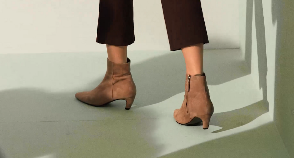 Ein Model sitzt auf einem stark vergrößerten Schuh von Bibi Lou. Der Schuh ist hellgelb mit einer goldnen Schnalle und offen im Fersenbereich