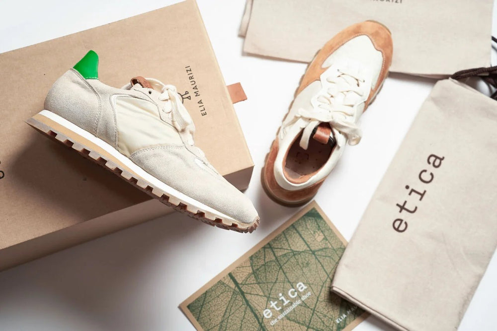 Ein Paar weiße Turnschuhe, die auf einer Schachtel liegen. Die Box hat die Aufschrift "Elia Maurizi"