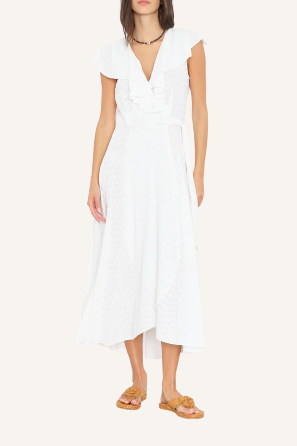 Weißes Wickelkleid mit fließender Silhouette, V-Ausschnitt mit mehrlagigen Rüschen, zarten Cap-Sleeves und Bindegürtel aus Oberstoff, getragen von einer Frau mit Sandalen