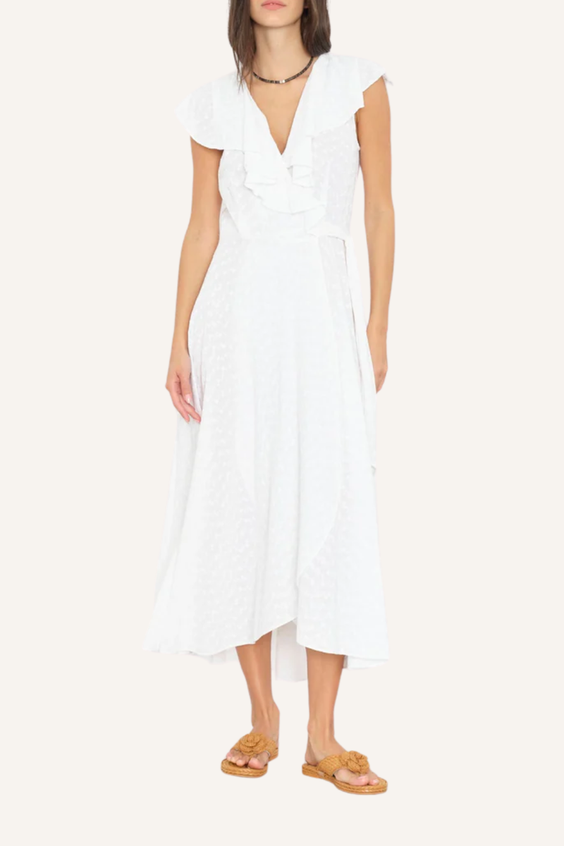Weißes Wickelkleid mit fließender Silhouette, V-Ausschnitt mit mehrlagigen Rüschen, zarten Cap-Sleeves und Bindegürtel aus Oberstoff, getragen von einer Frau mit Sandalen