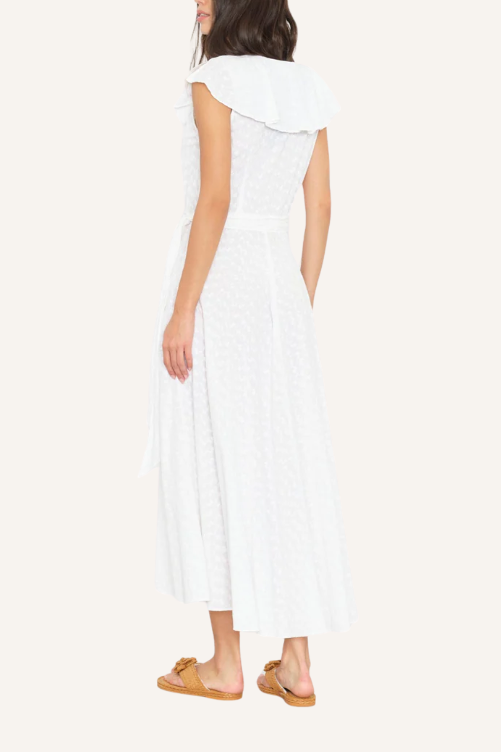 Weißes Wickelkleid mit fließender Silhouette, V-Ausschnitt mit mehrlagigen Rüschen, zarten Cap-Sleeves und Bindegürtel aus Oberstoff, getragen von einer Frau mit Sandalen