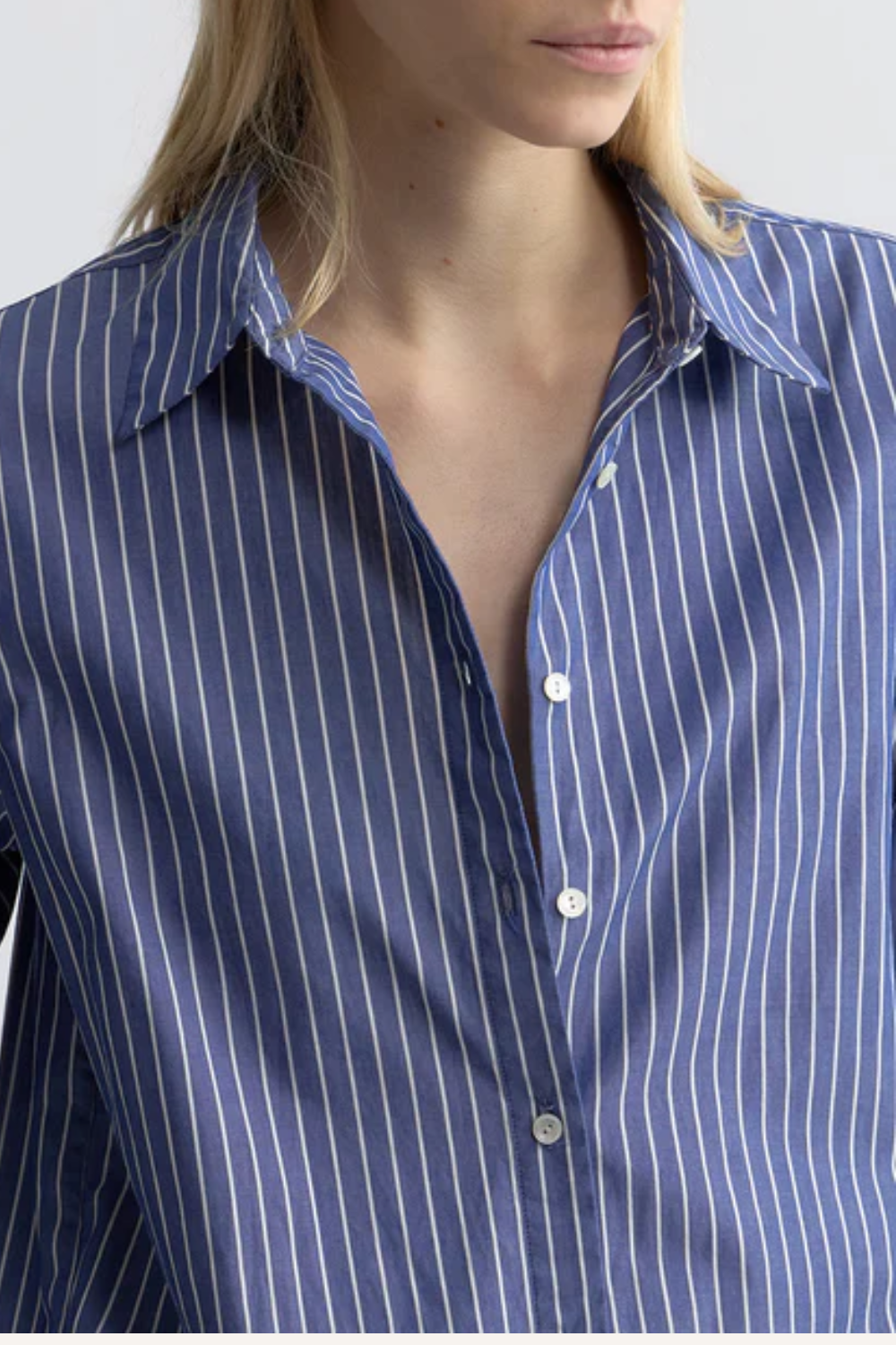 Frau trägt eine übergroße, blau-weiß gestreifte Hemdbluse aus italienischem Baumwoll-Popeline mit Knopfleiste vorne, Knopfmanschetten und verlängertem, abgerundetem Saum sowie extralockerer Passform