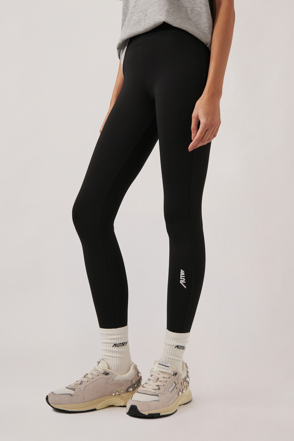 Frau trägt graues T-Shirt, schwarze Leggings mit hohem Bund und weiße Sportsocken mit hellen Sportschuhen