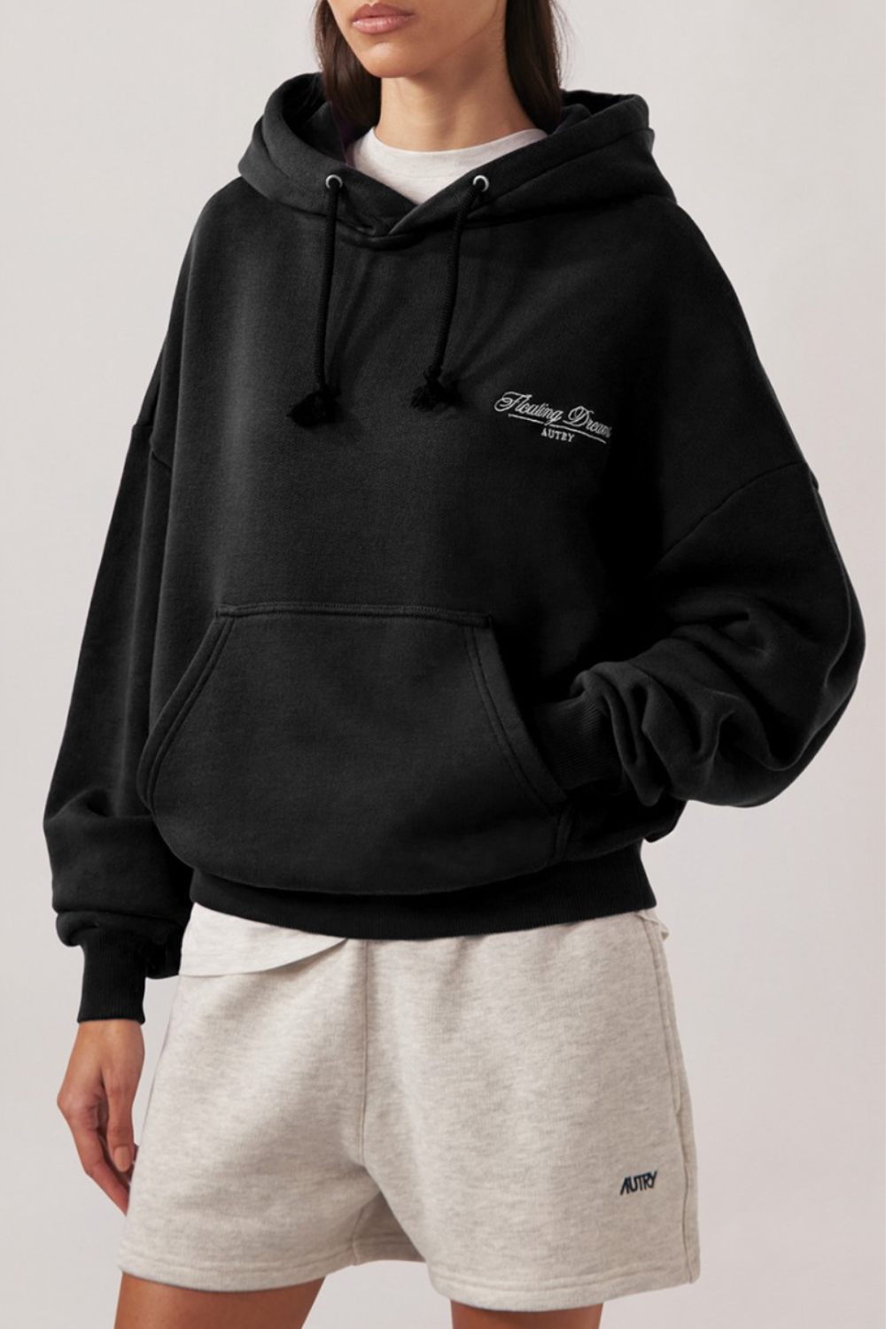 Schwarzer Hoodie aus Baumwolle mit Kordelzug und gerippten Bündchen, vorne kleine Stickerei mit Schriftzug, kombiniert mit hellen Shorts mit kleinem Logo.
