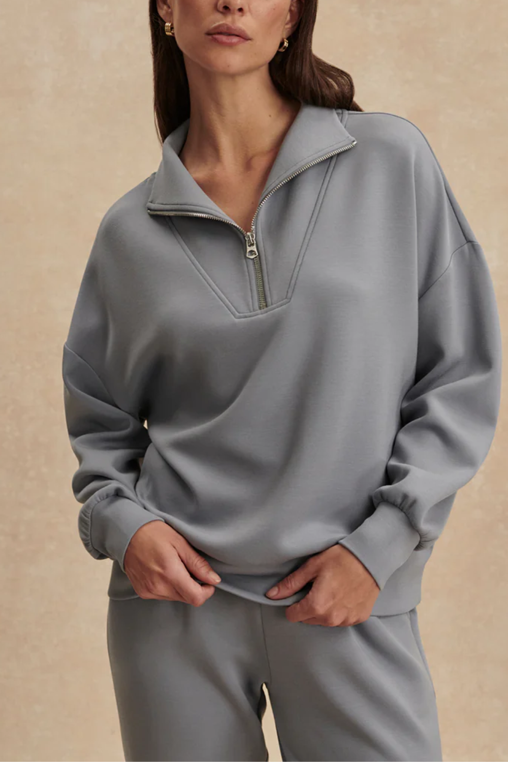 Frau trägt oversized Fit Sweatshirt mit halbem Reißverschluss, tiefen Ärmelbündchen und breitem Saumbund in babyblau