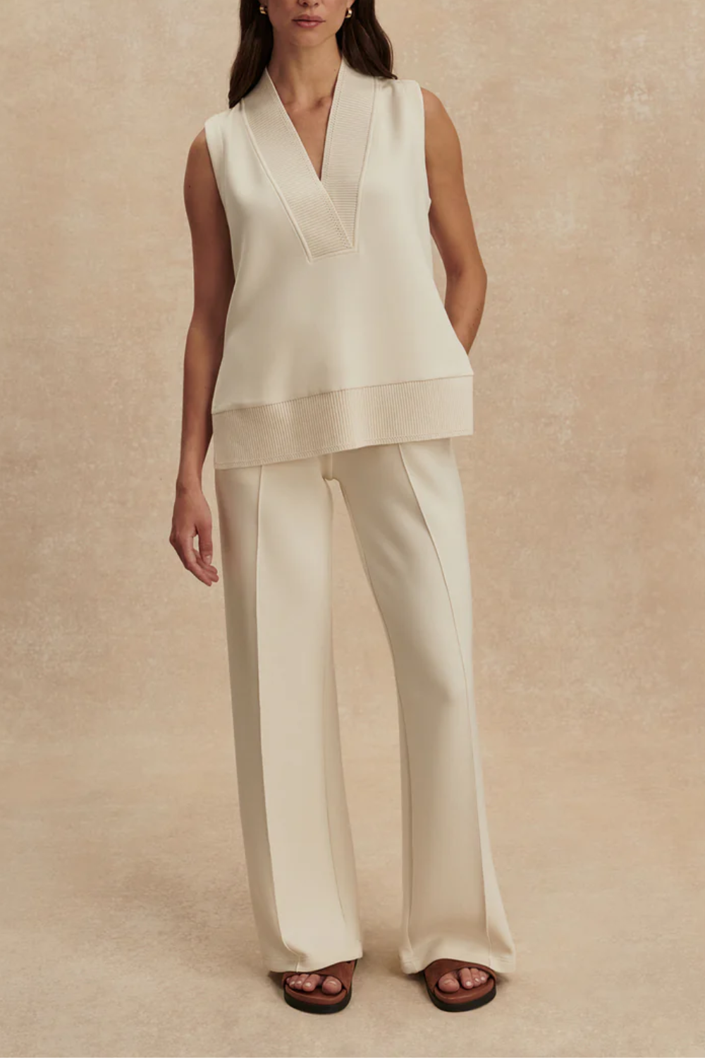 Ärmelloses Sweat-Top in Longline-Silhouette mit tiefem V-Ausschnitt, breitem Pointelle-Strickbündchen und seitlichen Schlitzen, getragen von einer Frau in entspannter Passform