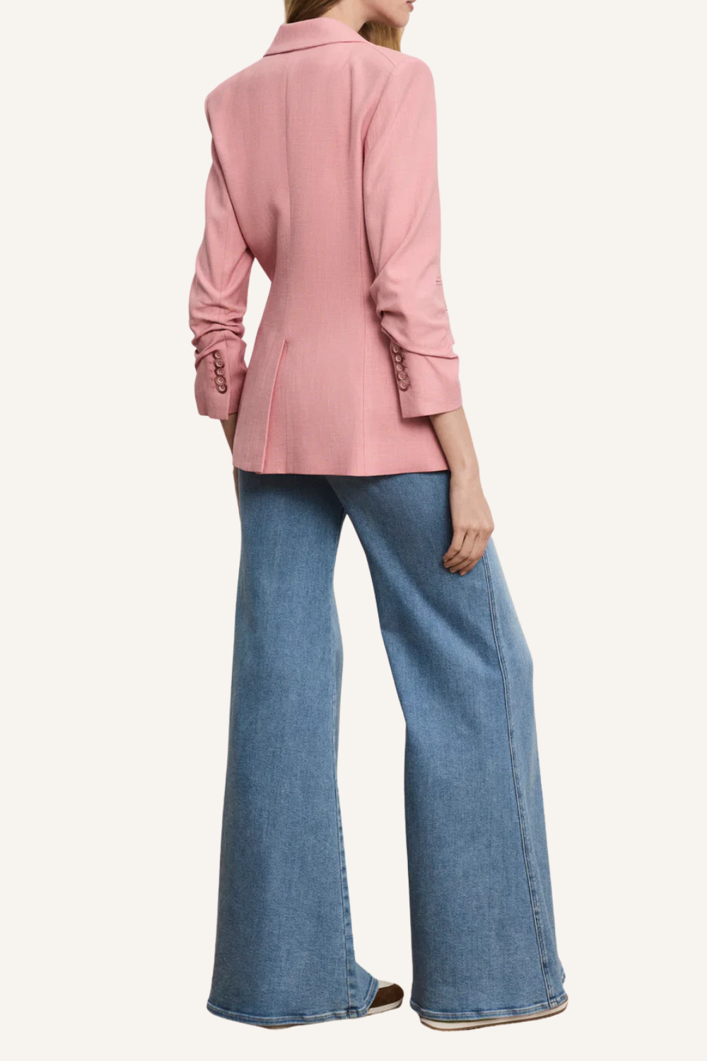 Einreihiges rosafarbenes Blazer-Modell mit klassischem Revers, vorgekräuselten Ärmeln und feiner Slub-Struktur, kombiniert mit weißem Top und blauen Jeans.