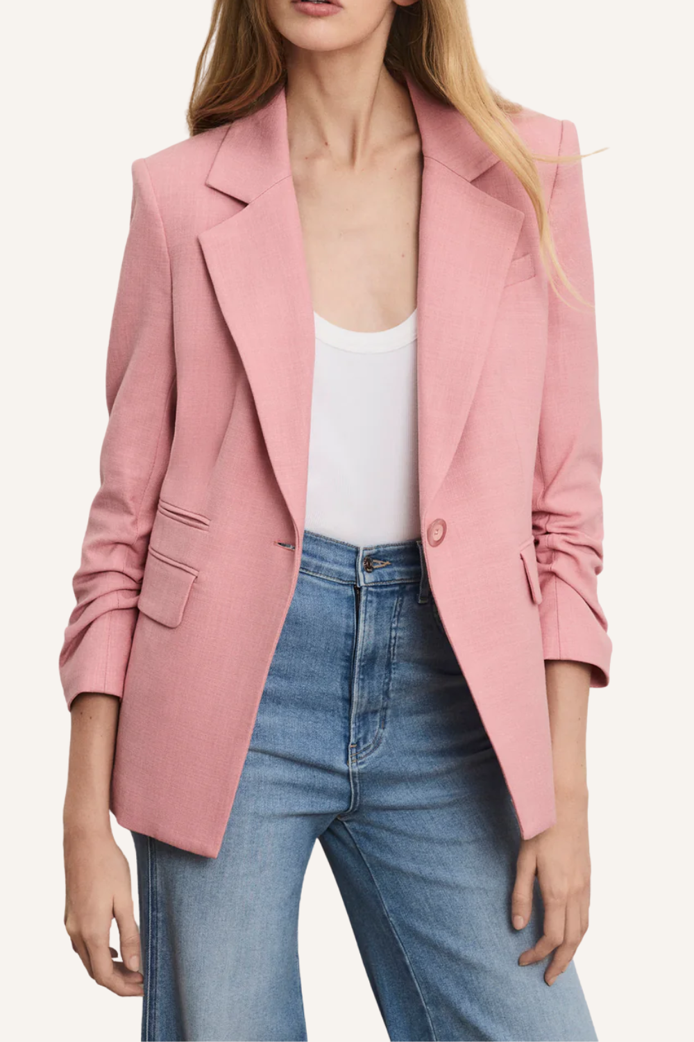 Einreihiges rosafarbenes Blazer-Modell mit klassischem Revers, vorgekräuselten Ärmeln und feiner Slub-Struktur, kombiniert mit weißem Top und blauen Jeans.