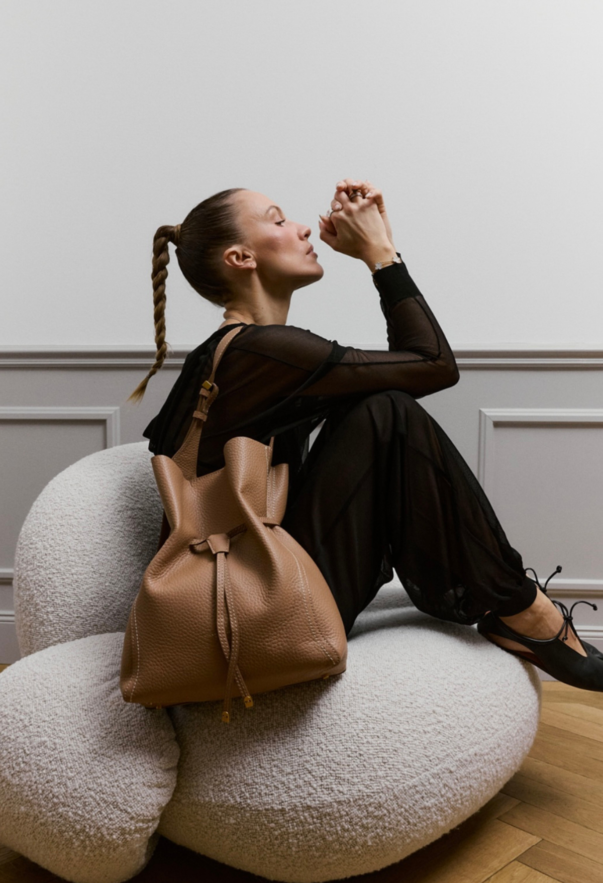 Model sitzt auf rundem Sessel mit beigem Leder-Beuttelrucksack mit Zugband, kombiniert mit schwarzem Transparenz-Top und schwarzer Hose – Damentaschen bei Marandino