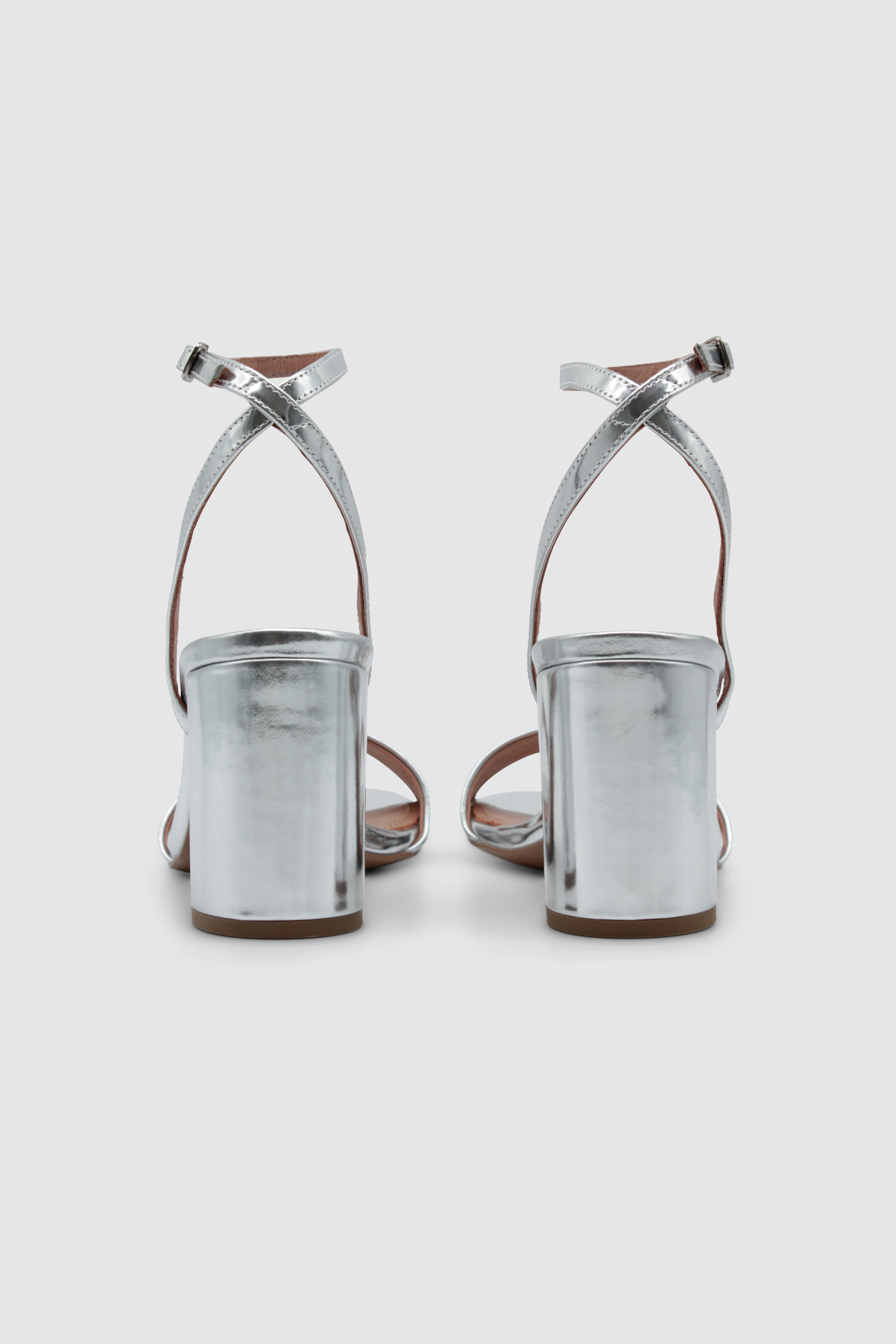 Silberne Sandalen mit einem Fesselriemen, der an der Ferse gekreuzt ist. Mit einem hohen, breiten Absatz. Von der Marke Bibi Lou