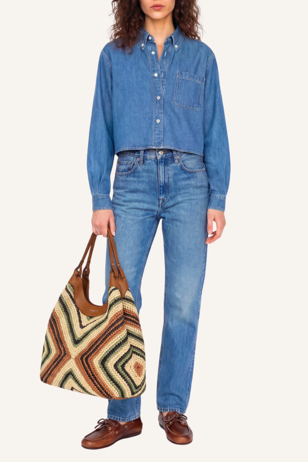 Frau in blauem Jeanshemd und Jeanshose hält geflochtene Strohtasche mit Lederkanten und doppelten Tragegriffen in der Hand