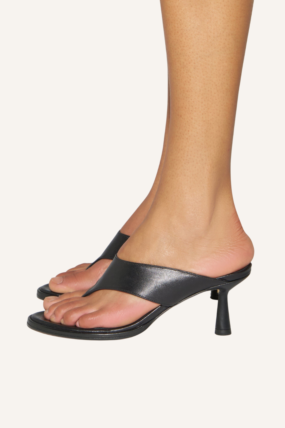 Schwarze Zehensandale mit breitem V-förmigem Riemen, Zehensteg und kantigem Stiletto-Absatz an einem Fuß