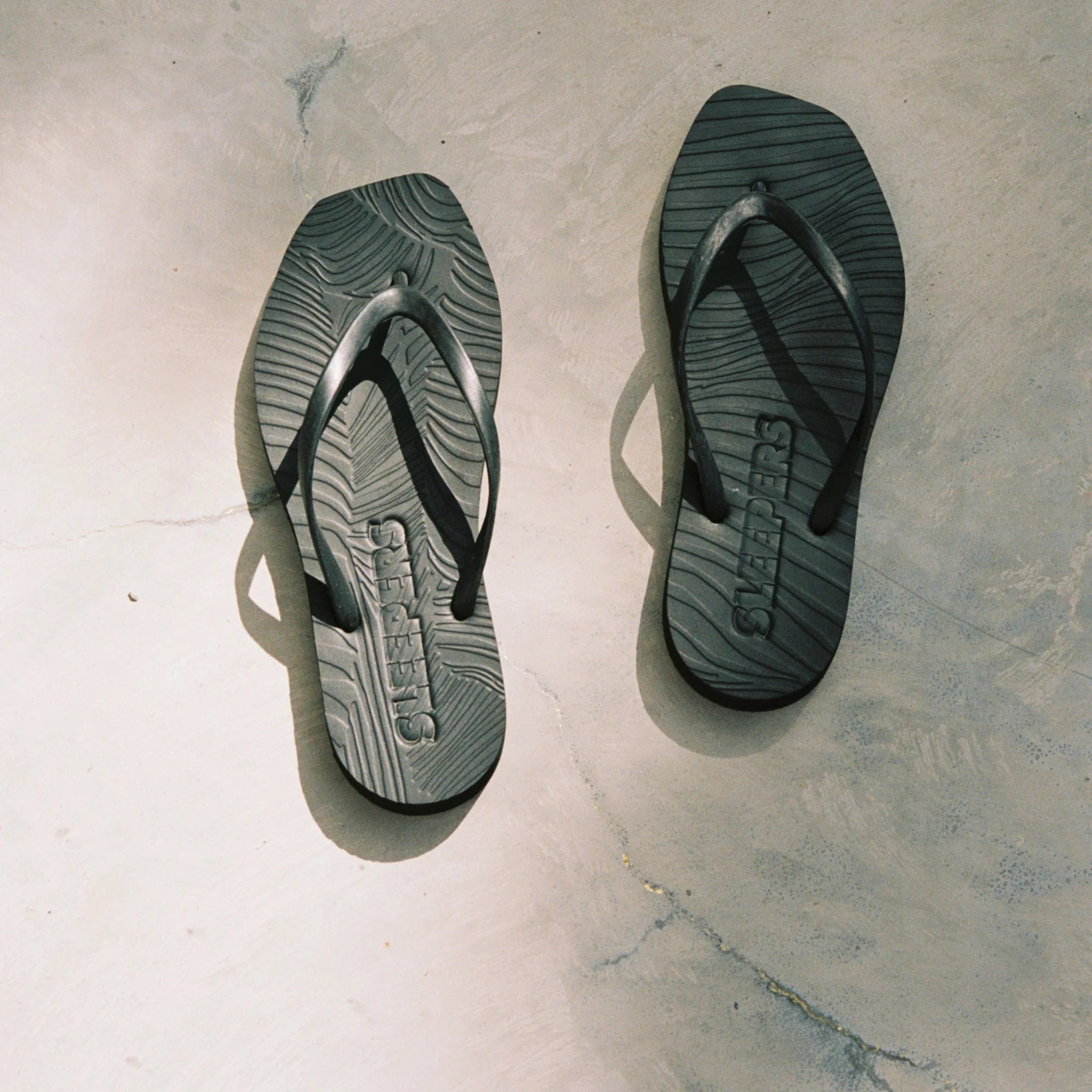 Schwarze Flip-Flops mit gewölbter Sohle und Riemen aus Naturkautschuk, mit dem Schriftzug 'SLEEPERS' auf der Innensohle