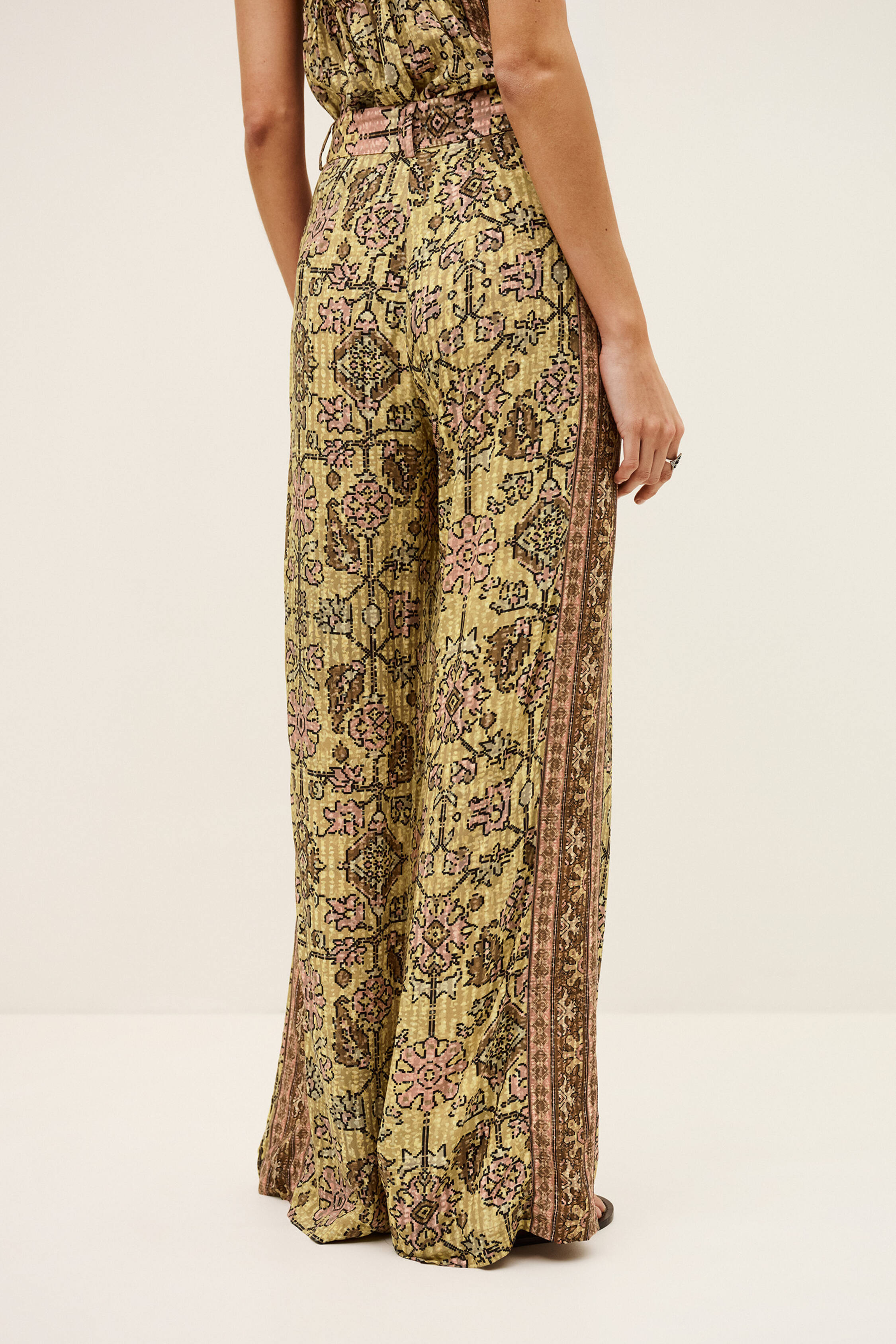Frau trägt weite Hose mit gemischtem Print, Hosenschlitz mit Reißverschluss, Metallhaken innen, Gürtelschlaufen und breitem Gürtel